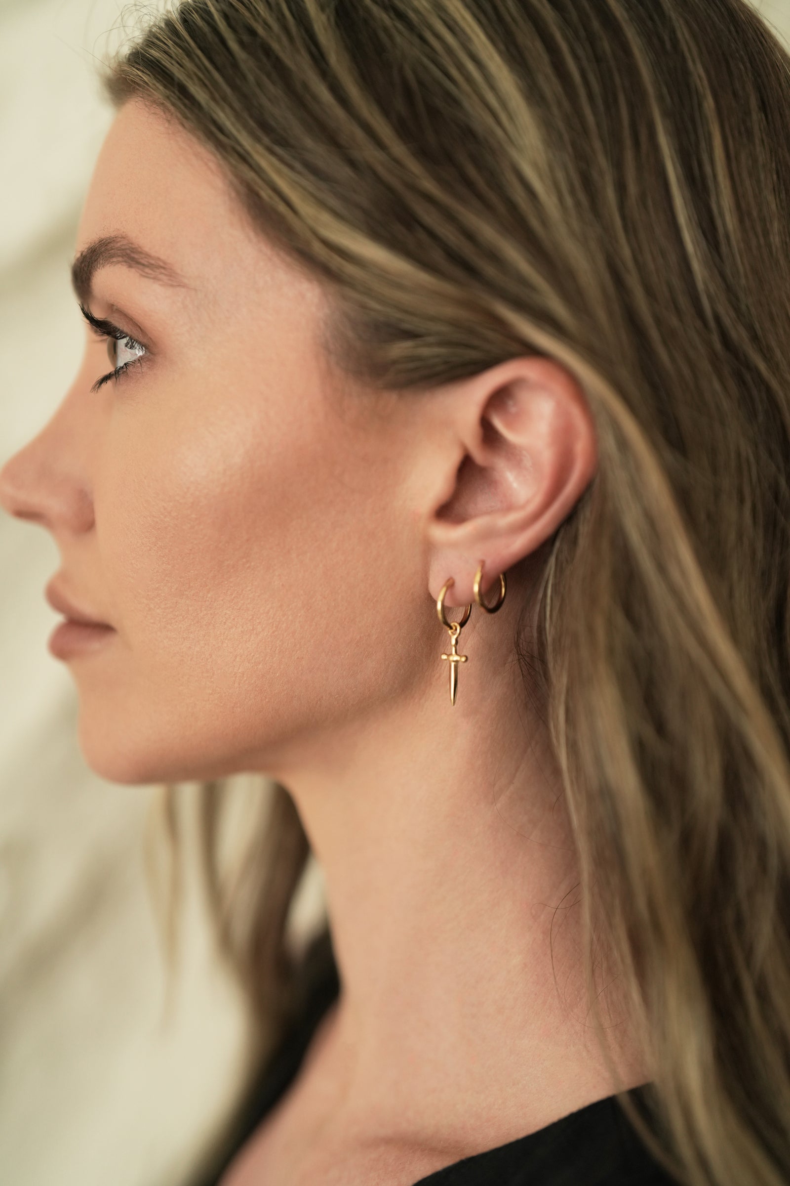Founder of Nusands Emily Micari side profile wearing 18k gold hoop earrings with removable sword charms in left ear