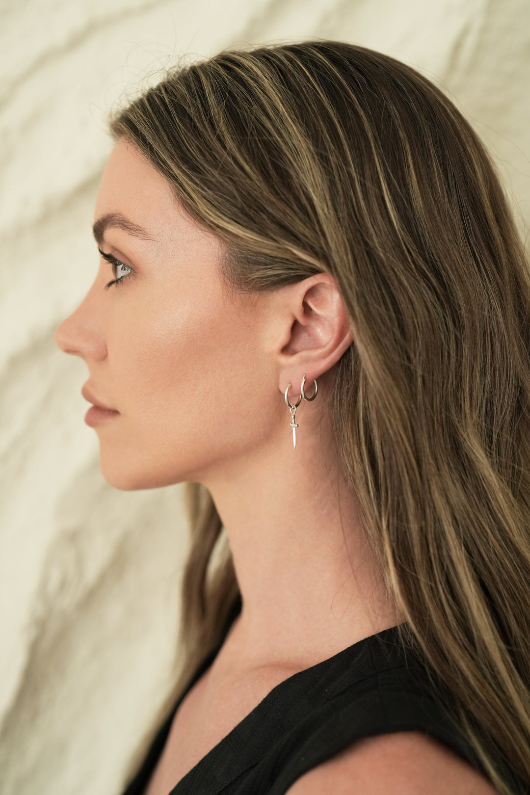 Founder of Nusands Emily Micari side profile wearing sterling silver hoop earrings with removable sword charm in left ear